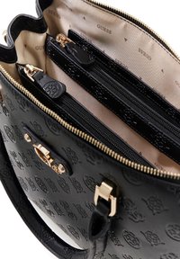 Sac à main en similicuir noir avec motif de logo embossé. Intérieur avec doublure beige et trois compartiments zippés. Accents de quincaillerie couleur or.