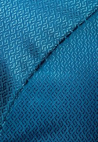 Getextureerde stof in tinten blauw, met een geometrisch patroon en een glanzende afwerking. Het oppervlak is glad met ingewikkelde details.