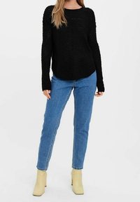 Maglione nero lavorato a maglia con un motivo testurizzato, scollo a barca e maniche lunghe, abbinato a jeans in denim blu e stivaletti beige alla caviglia.