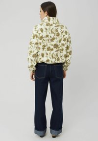 Veste en polaire avec un motif floral vert et violet sur un fond crème, associée à un jean large bleu foncé avec des ourlets retournés.
