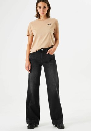 T-shirt en coton beige avec un graphique brodé et un pantalon large noir. La tenue présente une coupe décontractée et un design minimaliste.
