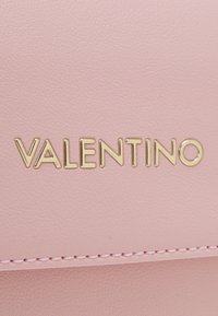 Różowy skórzany portfel z teksturowaną powierzchnią, złotym logo "VALENTINO" oraz subtelnym przeszyciem wzdłuż krawędzi.