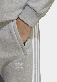 Grau Baumwollpullover mit einer Tasche und weißem Adidas-Logo. Verfügt über drei weiße Streifen entlang der Seite und gerippte Bündchen.