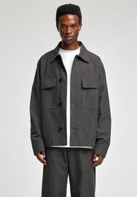 Szara marynarka w prążki z kołnierzem, dwoma przednimi kieszeniami i luźnym krojem, zestawiona z białą koszulą. Gładka faktura.