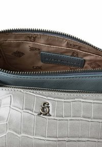 Szara torebka z imitacji krokodylej skóry z czarnym zamkiem. Wnętrze wyłożone jest brązową podszewką z wzorem logo i niebieską metką.