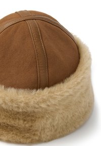 Bruine suede hoed met een ronde vorm, voorzien van een tan nepbont rand. Het ontwerp heeft gestikte lijnen en een zachte textuur.