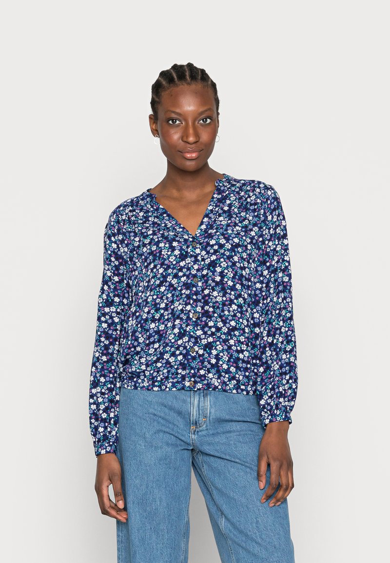 Blusa azul-marinho floral com mangas longas, decote em V e fecho com botão. Apresenta pequenas flores brancas e rosas numa tela texturizada.