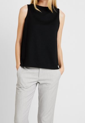Zwart mouwloos topje met een gestructureerde afwerking, voorzien van een hoge halslijn en een losse pasvorm, gecombineerd met lichtgrijze op maat gemaakte broeken.