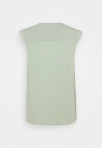 Haut sans manches vert clair en tissu doux, avec des accents en dentelle festonnée sur les épaules et un col rond.