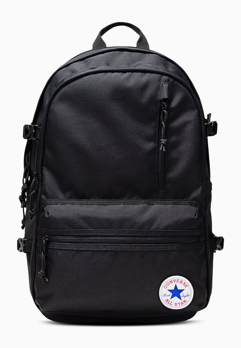 Mochila de tela negra con múltiples compartimentos con cremallera, espalda acolchada, asa en la parte superior y un parche redondo "Converse All Star".