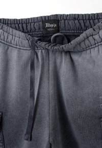 Pantaloni della tuta grigi con vita elasticizzata, cordino e tasche laterali. Texture liscia con una sfumatura sottile e etichetta "Utopia".