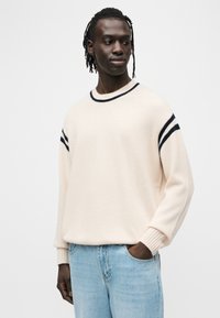 Πουλόβερ κρεμ με ριγέ σε σκούρο μπλε στις μανσέτες και το λαιμό. Μαλακή υφή, άνετη εφαρμογή και ριμπ μανσέτες, συνδυασμένο με ανοιχτόχρωμο μπλε τζιν.