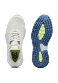 Tênis atléticos brancos com um cabedal texturizado, apresentando detalhes em azul e verde. Solado azul com padrão de cravos e inserções de amortecimento verdes para tração.