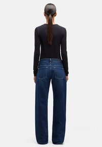 Szerokie spodnie dżinsowe w kolorze ciemnoniebieskim z wysokim stanem, z tylnymi kieszeniami i gładką, fakturowaną powierzchnią. Połączone z czarną bluzką z długim rękawem.