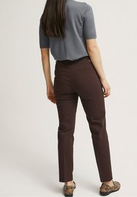 Bruna skräddarsydda byxor i slät väv, med slim fit, två bakfickor, och en grå kortärmad topp. Skorna har snakeskin-mönster.