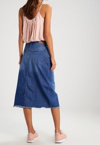 Falda midi de denim con dobladillo deshilachado, con bolsillos laterales y cintura de altura media. Combinada con una blusa sin mangas de color rosa claro y calzado casual.