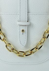 White textured leather bag with a gold chain strap. Features a central flap with a button closure and visible stitching details.