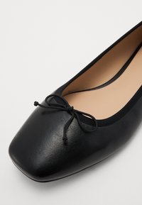 Bailarinas de cuero negro con puntera redondeada, que presentan un pequeño lazo en la parte frontal y una superficie texturizada. Forro interior suave.
