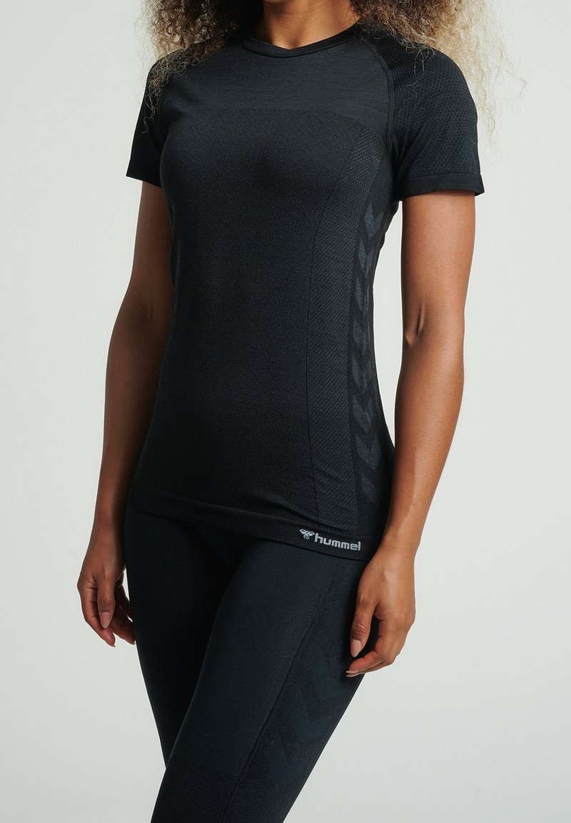 Top atlético negro de manga corta, con tejido texturizado y un sutil logotipo. Combinado con leggings negros que presentan un patrón de chevron en los laterales.