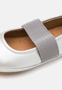 Ballerina in pelle argentata con una fascia elastica grigia sopra il collo del piede, dotata di una soletta beige e dettagli cuciti lungo il bordo.