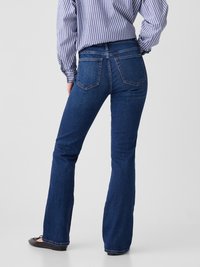 Flared dark blue denim jeans with standard back pockets, subtle stitching details, and a smooth texture, paired with a blue and white striped shirt.