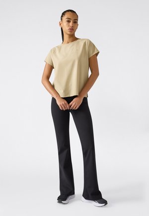 Top beige a maniche corte con vestibilità morbida, abbinato a pantaloni neri svasati e scarpe sportive nere con suole bianche.