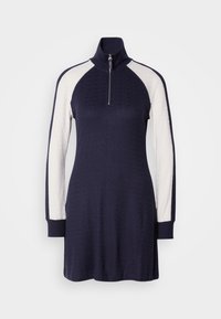 Robe en maille avec col montant et fermeture éclair frontale, corps bleu marine avec manches raglan longues blanches contrastantes et poignets côtelés.
