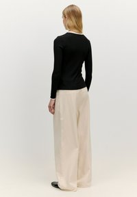 Zwarte geribbelde langärmige top met een witte kraag, gecombineerd met beige wijde broekspijpen. Gladde textuur, eenvoudig ontwerp, geen patronen of accenten.