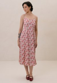 Różowa sukienka kwiatowa z cienkimi ramiączkami, w fasonie A-line, uszyta z lekkiego materiału. Charakteryzuje się małymi czerwonymi kwiatkami i zielonymi liśćmi w rozproszonym wzorze.
