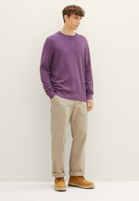 Maglione lungo a maniche lunghe viola a coste abbinato a pantaloni cargo beige e stivali gialli, caratterizzati da polsini alla caviglia e un design diritto.
