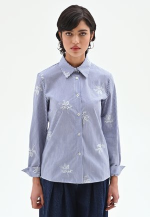 Chemise à rayures bleu et blanc à manches longues, avec boutons sur le devant et accents de broderie florale sur la poitrine et les manches. Matière en coton.