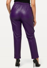 Pantalons en simili cuir violet avec une taille élastique, design à jambes fuselées et finition brillante, associés à des chaussures à talons hauts noires.