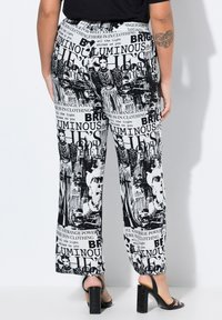 Zwarte en witte wijde broekspijpen met een grafische print met tekst en afbeeldingen, gemaakt van lichtgewicht stof met een elastische tailleband.