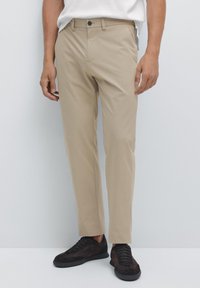 Beige skräddarsydda byxor med en mjuk textur, utrustade med knappstängning och sidofickor, matchade med mörkbruna sneakers.