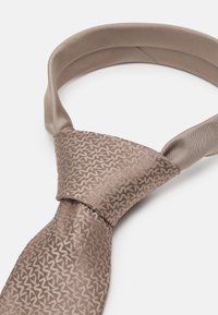 Brun silke slips med et geometrisk mønster, som har en glatt tekstur og en ensfarget, bredere bånd rundt halsen.