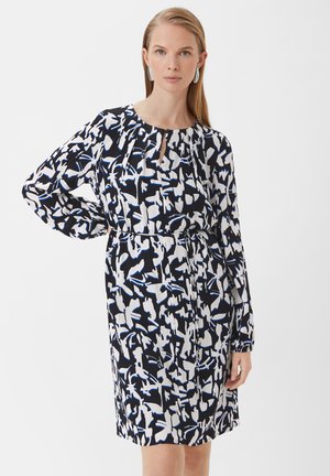 Zwart-wit gestreepte jurk met blauwe accenten, lange mouwen, en een sleutelgat halslijn, en een getailleerde taille. Glad materiaal met een relaxte pasvorm.