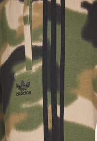 Maskáčová mikina v zelených, béžových a černých odstínech s třemi černými pruhy a vyšitým černým logem Adidas.