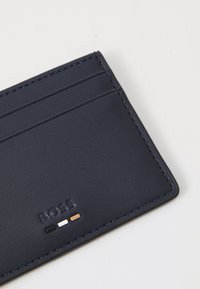 Navy leather cardholder with embossed "BOSS" logo and three accent dots in black, white, and gold. Features multiple card slots.