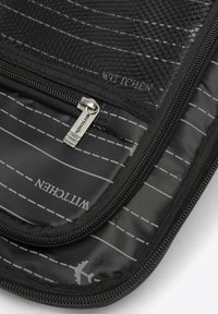 Černá zipová úložná taška s síťovanou texturou, zdobená bílými diagonálními pruhy a malou grafikou letadla. Logo viditelné uvnitř.