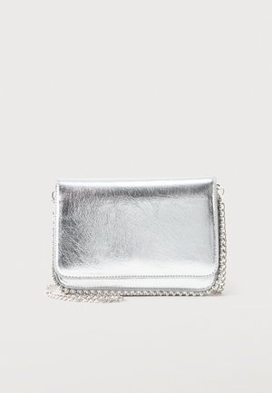 Petit sac métallique rectangulaire argenté avec une bandoulière chaîne reposant sur une surface claire, rabat fermé face vers l'avant.