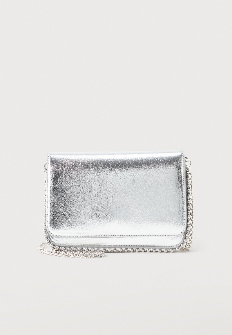 Petit sac métallique rectangulaire argenté avec une bandoulière chaîne reposant sur une surface claire, rabat fermé face vers l'avant.