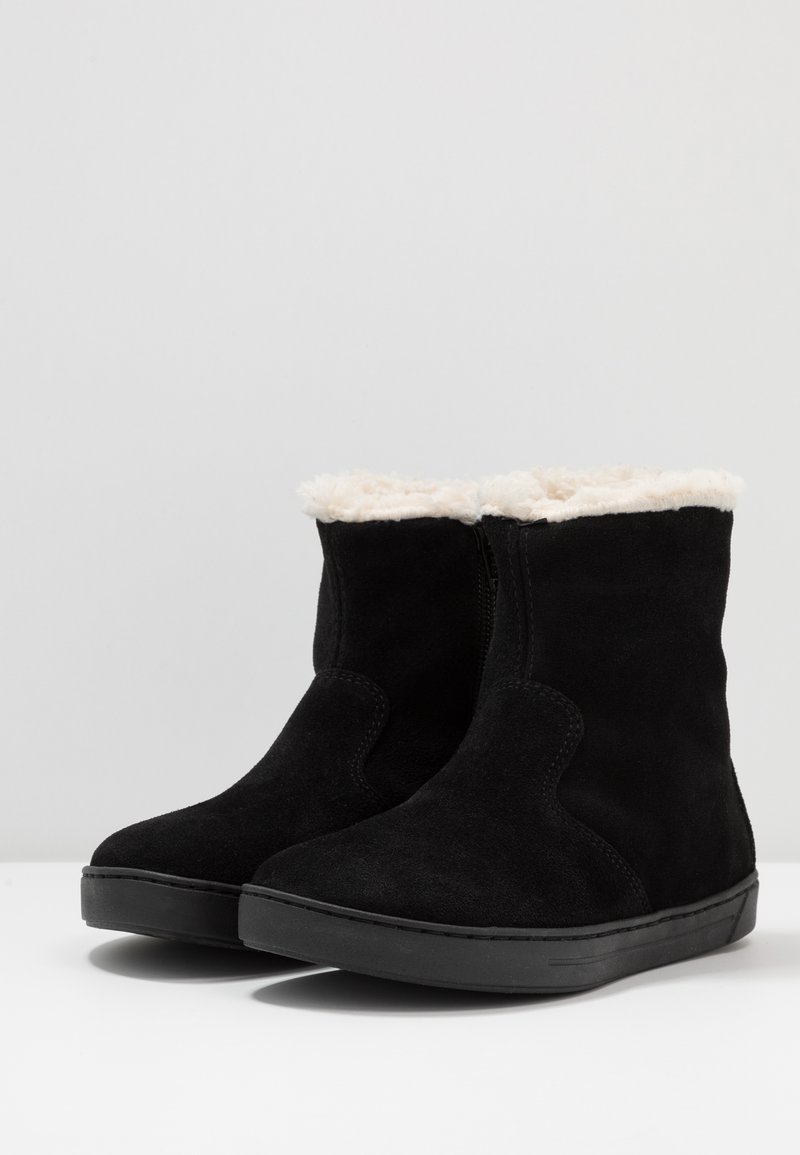 Schwarze Wildleder-Ankle Boots mit einem cremefarbenen Fellfutter und einer flachen schwarzen Sohle; ausgestattet mit einem seitlichen Reißverschluss für ein einfaches Anziehen und einem glatt gerundeten Zehendesign.