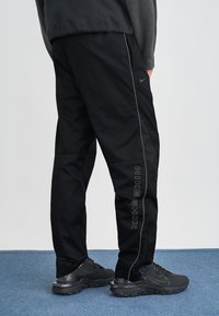 Mustad musta Nike Shox'i püksid, millel on kitsenev disain, peegeldavad detailid ja vertikaalne logo külje peal. Materjal näeb välja kerge.