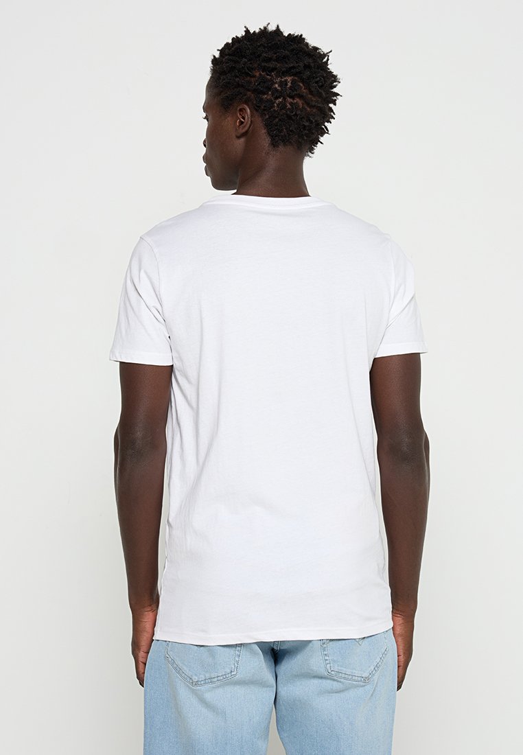 Biała bawełniana koszulka z okrągłym dekoltem, krótkimi rękawami i luźnym krojem, widoczna z tyłu. Połączona z jasnoniebieskimi dżinsami.