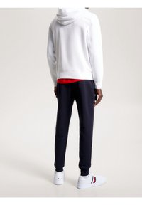 Sudadera blanca con capucha combinada con una camisa roja y pantalones de chándal azul marino, con puños elásticos, y zapatillas blancas con una franja de color.