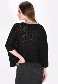 Maglione nero lavorato a maglia con design a traforo, caratterizzato da un ampio scollo e maniche corte. Abbinato a una gonna in denim scuro.