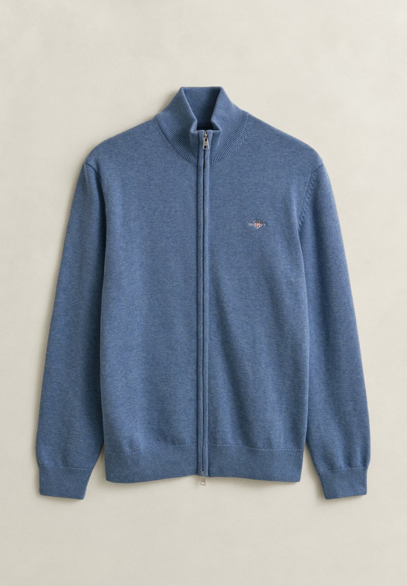 Maglione blu a manica lunga con cerniera integrale, polsini e collo a coste, piccolo logo ricamato sul petto sinistro, disteso su uno sfondo chiaro.