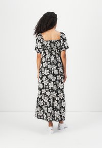 Sort blomster maxi kjole med hvide hibiscus mønstre, firkantet halsudskæring, korte puff ærmer og lagdelt kant. Båret med hvide sneakers.