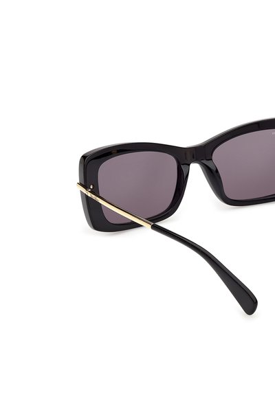 Lunettes de soleil rectangulaires noires avec des verres foncés et des détails dorés sur les branches, vues en gros plan sur un fond blanc.