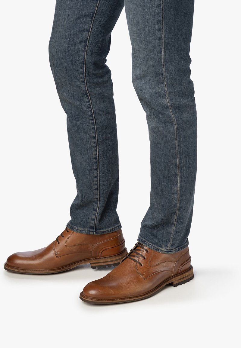 Bruine leren dresschoenen met een gladde afwerking, ronde neus en vetersluiting, gecombineerd met donkerblauwe denim jeans met een slim fit.